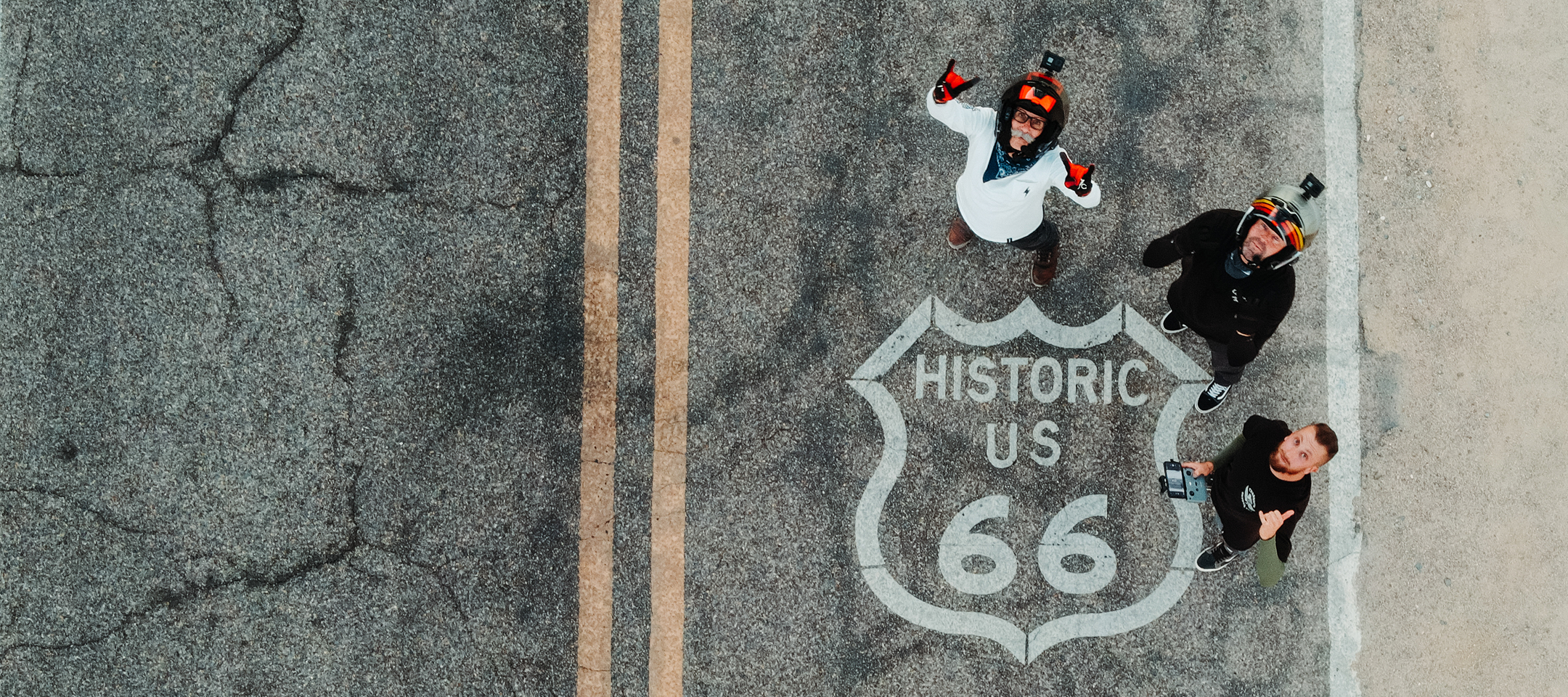 The 2LaneLife crew standing on a Route 66 road marking looking up, seen from a drone directly above