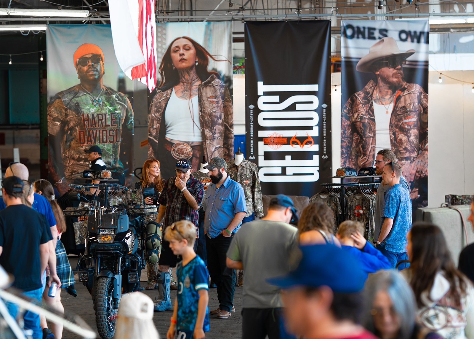 Crowds browse Harley-Davidson x Realtree apparel displays under giant “GET LOST” campaign banners at The Congregation Vintage Motorcycle Show.