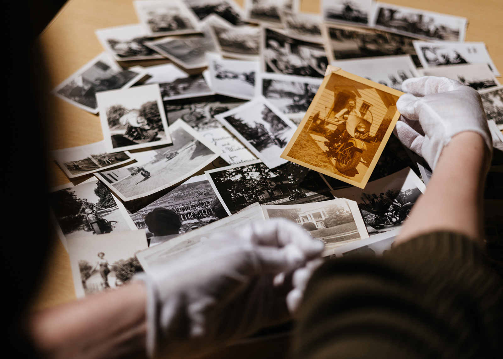 Looking over the shoulder of a Harley-Davidson museum curator with a large collection of vintage photographs on the table in front of them.