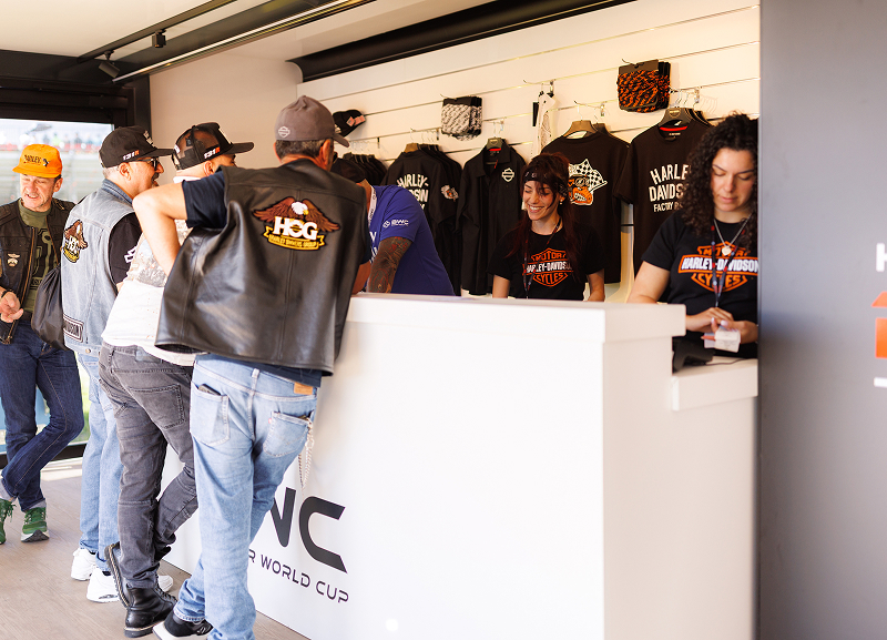 Visitors gather at a Harley-Davidson merchandise booth, browsing apparel and speaking with staff