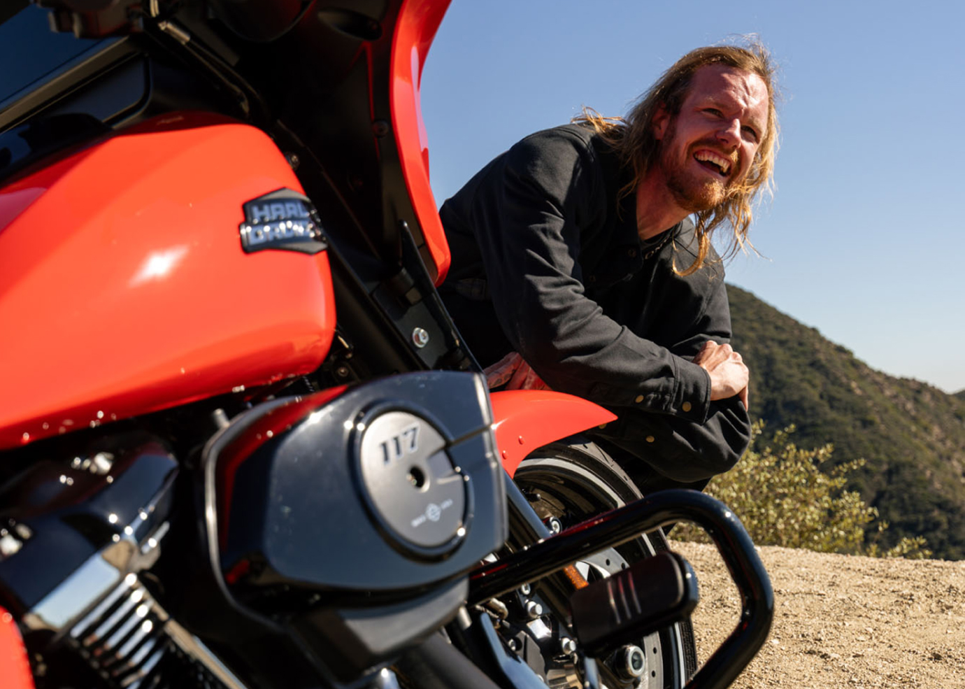 Pessoa encostada em uma motocicleta HD vermelha em um mirante de terra