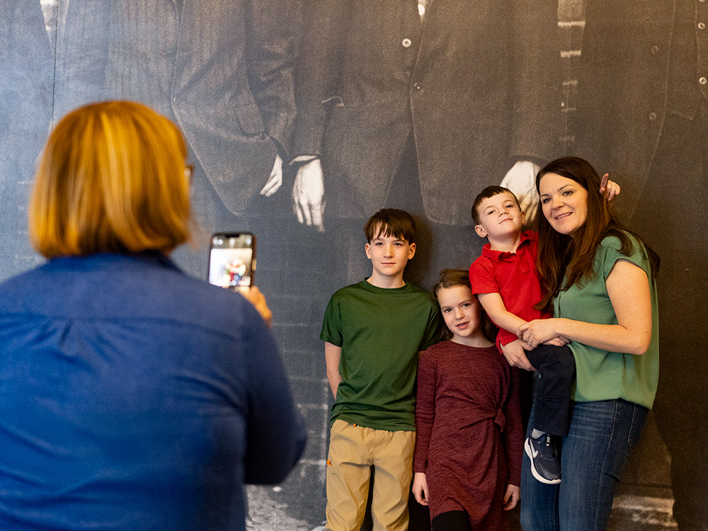 Group posing for photo in front of large historic portrait wall