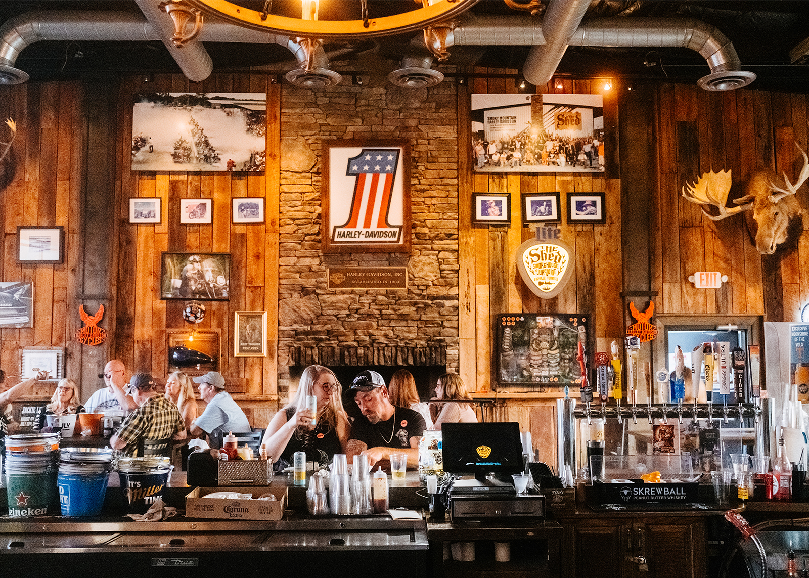 A couple along with others enjoying some food and drinks inside the rustic atmosphere of The Shed bbq.