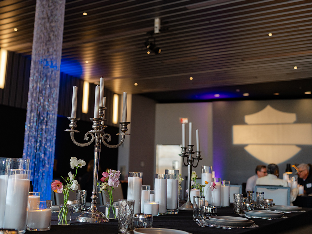 Event table setup with candles, floral accents, and stage screen in background