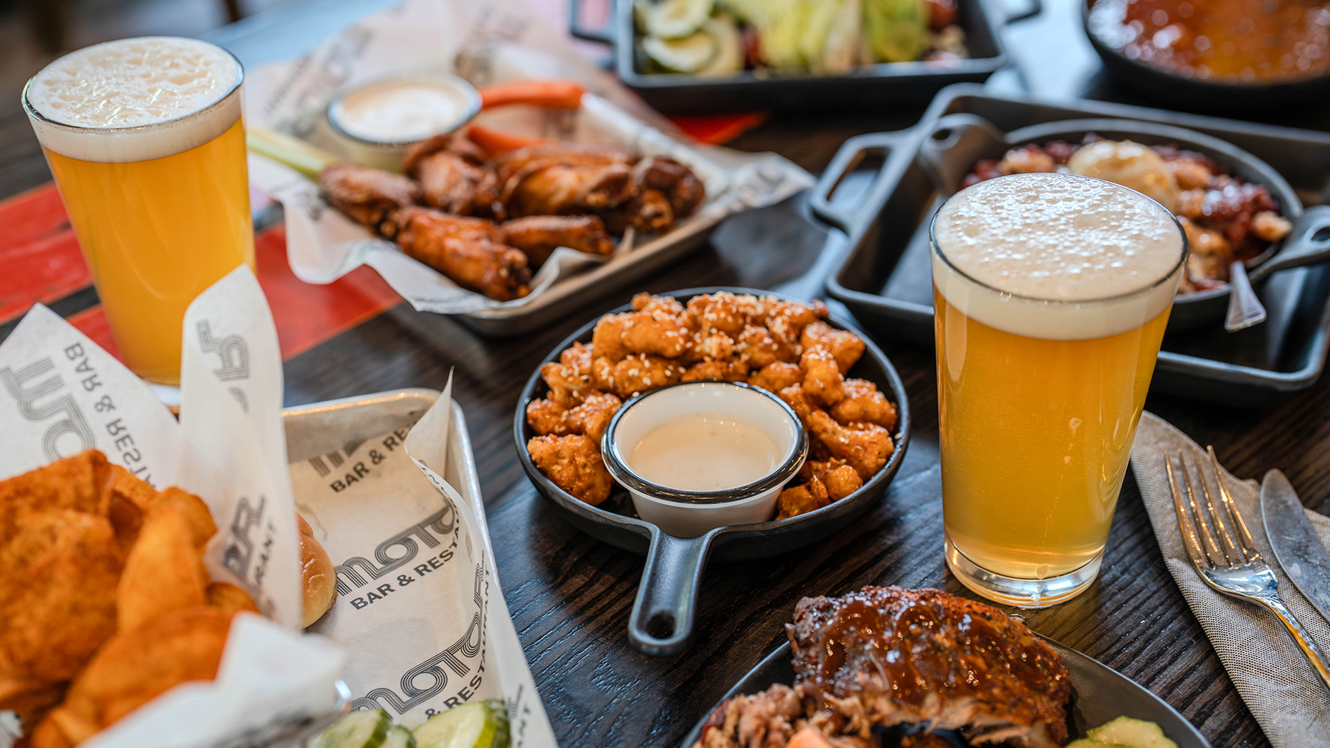Beer glasses and assorted appetizers including wings, pretzels, and chips on table