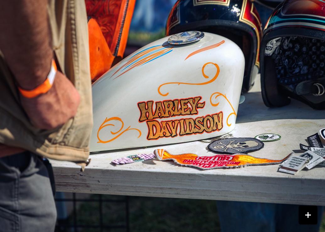 Close-up of a custom Harley-Davidson tank with detailed artwork displayed at a bike event