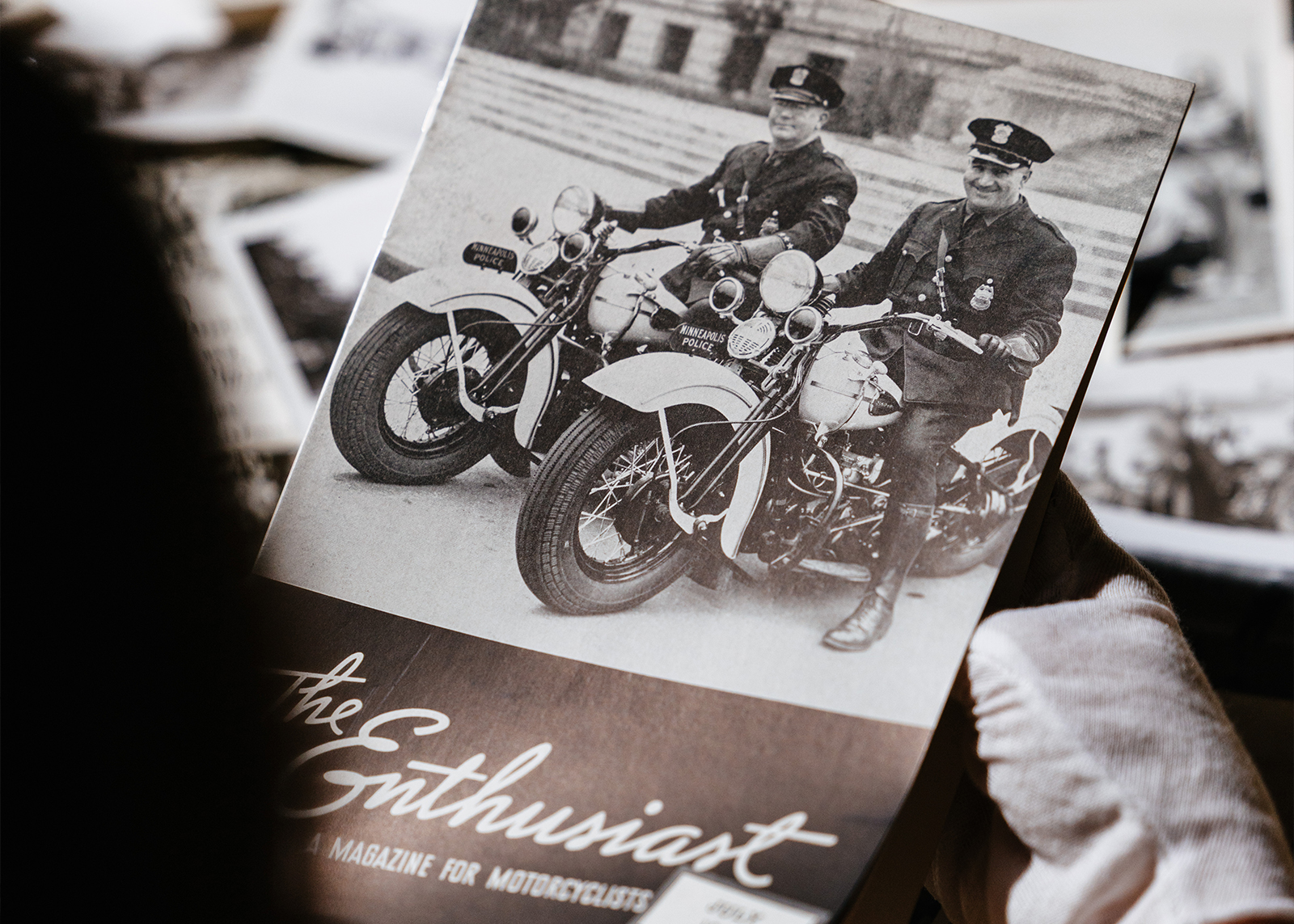 Looking over the shoulder of a Harley-Davidson museum curator holding a vintage copy of The Enthusiast magazine.