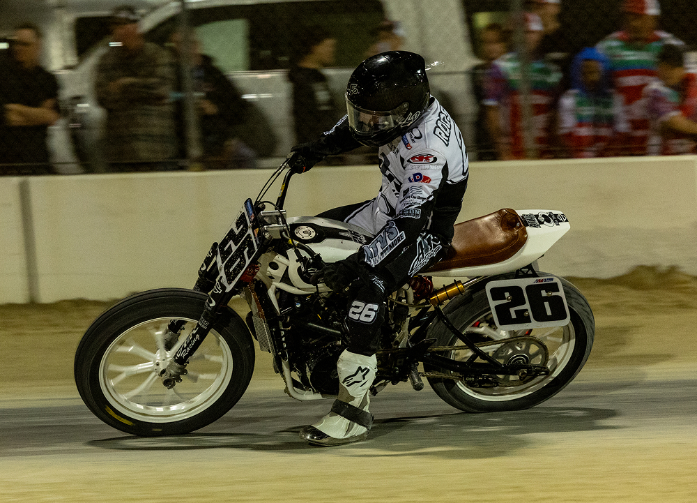 Flat track rider aboard motorcycle No. 26 powers through a dirt-track corner during a nighttime race