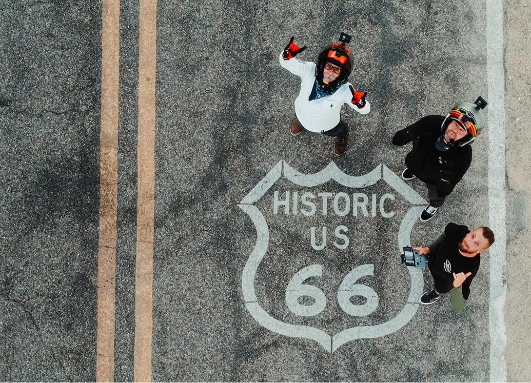 The 2LaneLife crew standing on a Route 66 road marking looking up, seen from a drone directly above