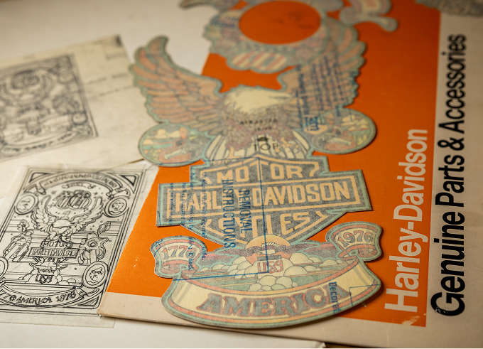 A decal of the eagle‑themed ‘76 Bicentennial artwork alongside a vintage Harley-Davidson parts catalog
