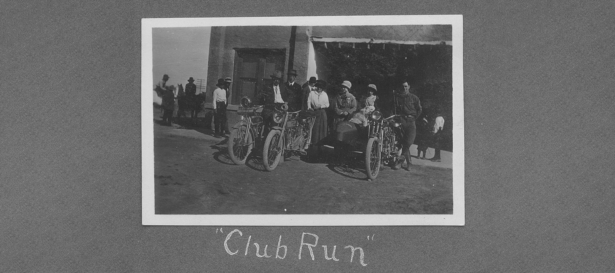 Vintage photograph labeled “Club Run” showing early motorcycles and riders gathered outside a building with spectators nearby