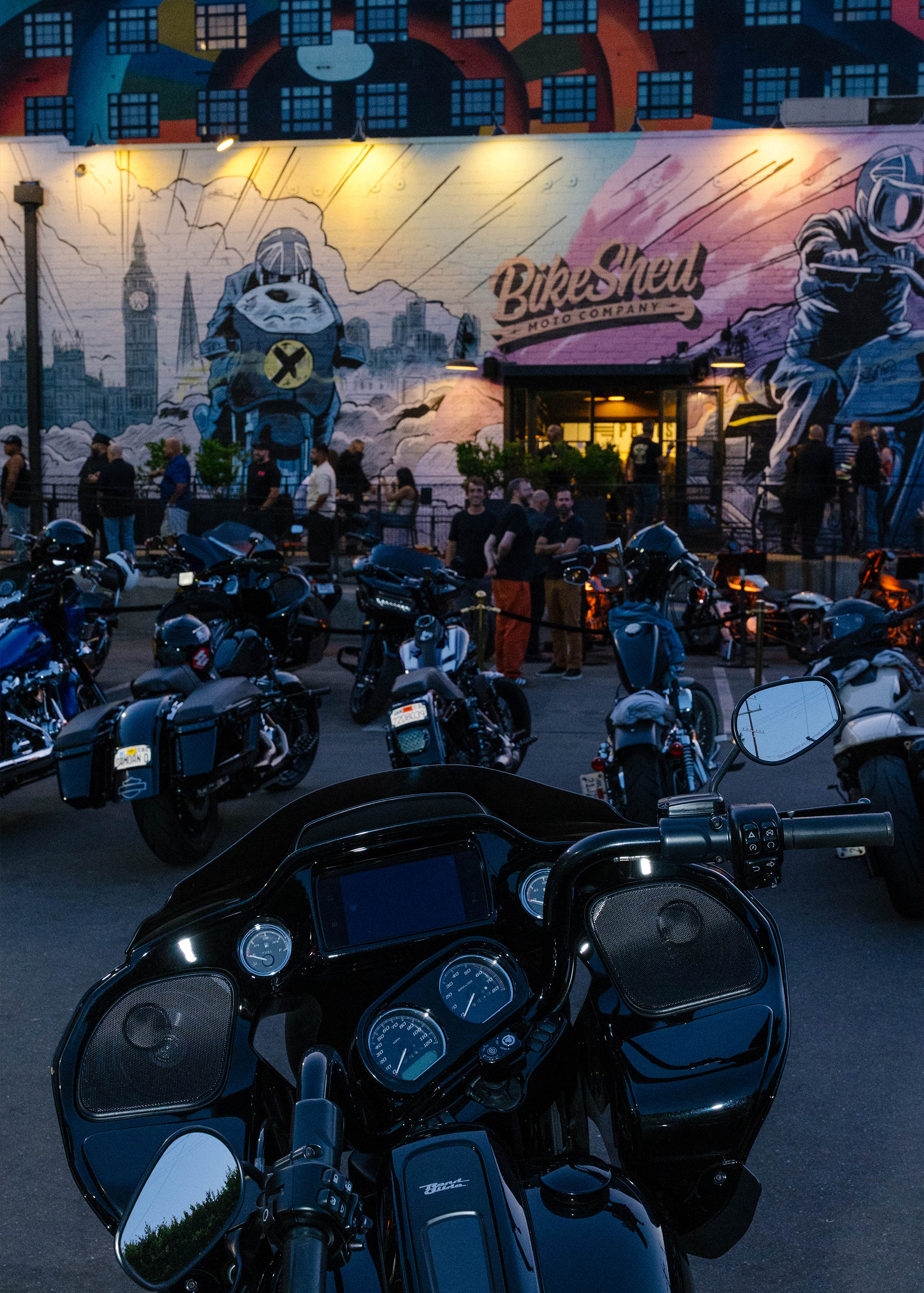 Motorcycles parked in front of Bike Shed Moto Company with a vibrant mural and people gathering outside.
