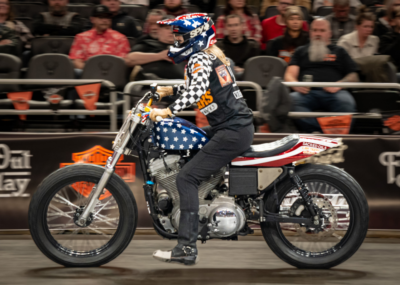 A woman rides an American flag-themed motorcycle on the indoor race track