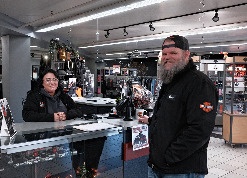 Two employees smile standing on either side of a counter in the showroom of Kegel Harley-Davidson