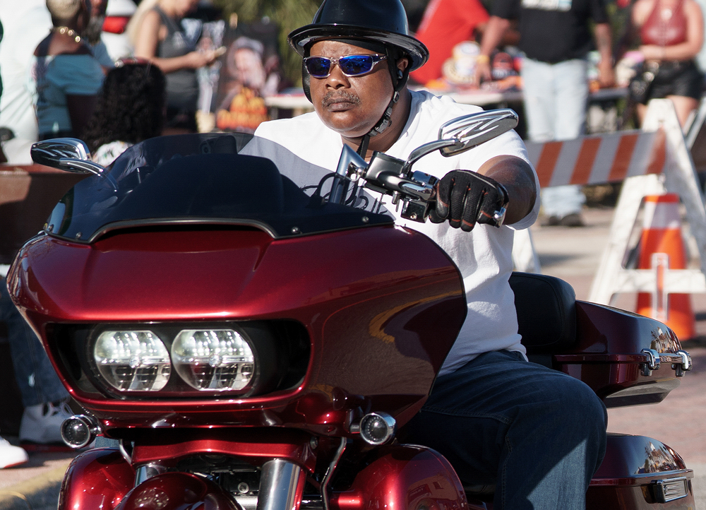 Rider on a red touring motorcycle stopped along a city street lined with onlookers and other bikes