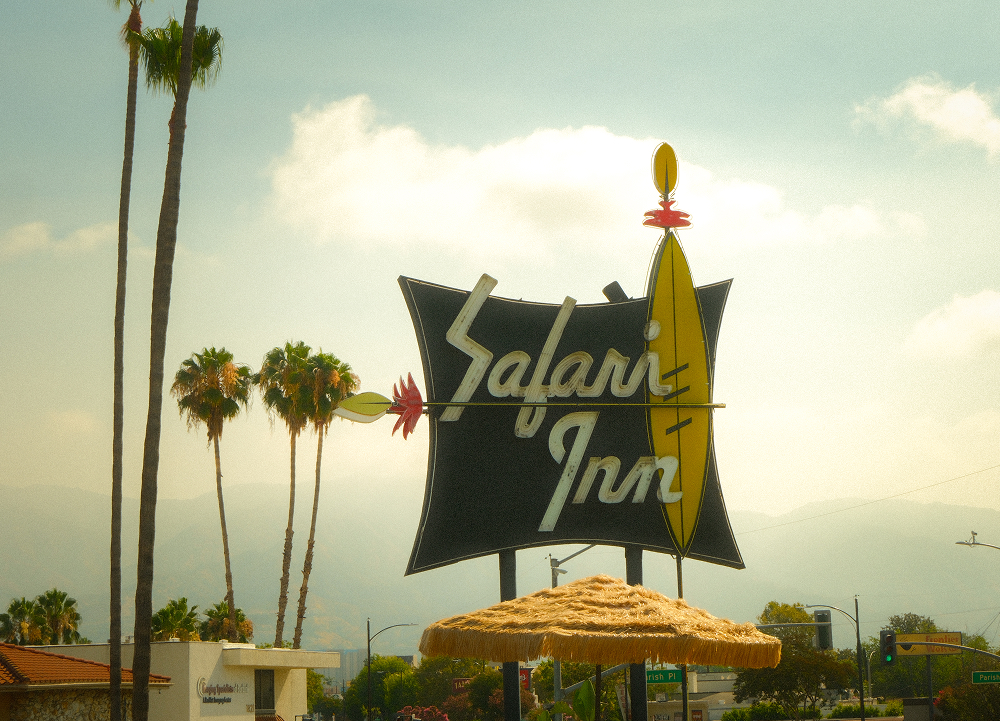 Vintage Safari Inn roadside sign with surfboard motif, palm trees, and mountains visible in the background