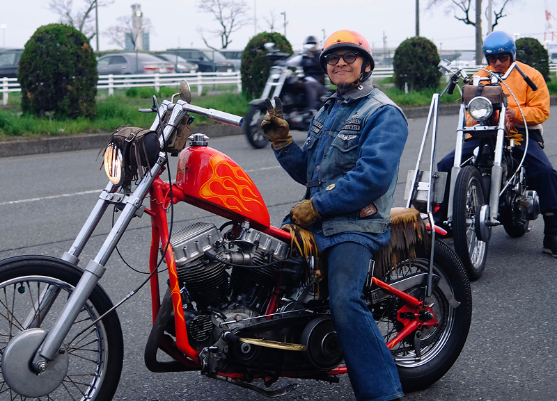 Rider on an orange custom chopper stopped on a roadside with another motorcycle and rider following behind