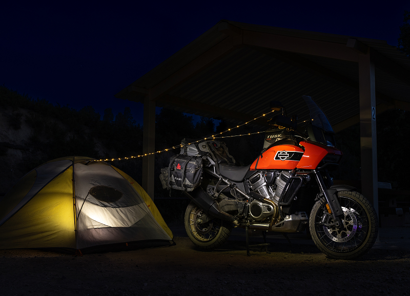 Red H-D Pan America motorcycle parked beside a lit tent at night under shelter, with string lights overhead