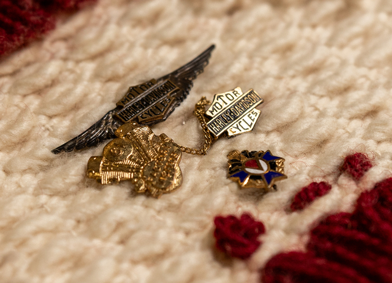 Close-up of vintage Harley-Davidson pins and badges arranged on textured fabric, showing detailed metalwork and color