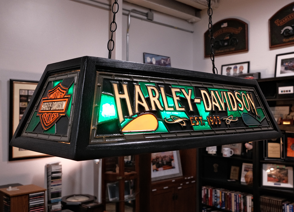 Close-up of illuminated Harley-Davidson stained glass hanging light with logo in dealership interior setting