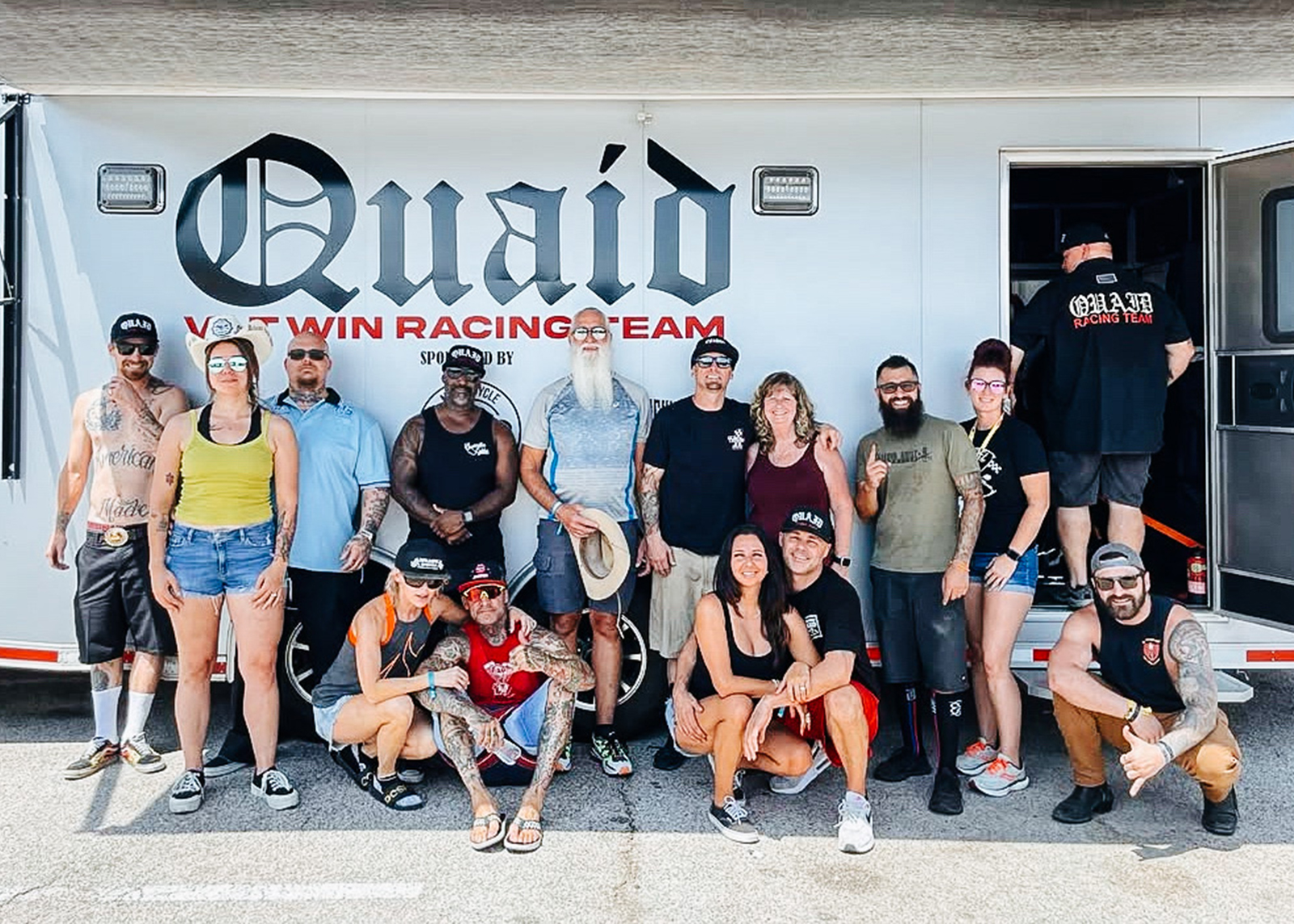 A group shot of the Quaid racing family in front of one of their trailers at a race track.