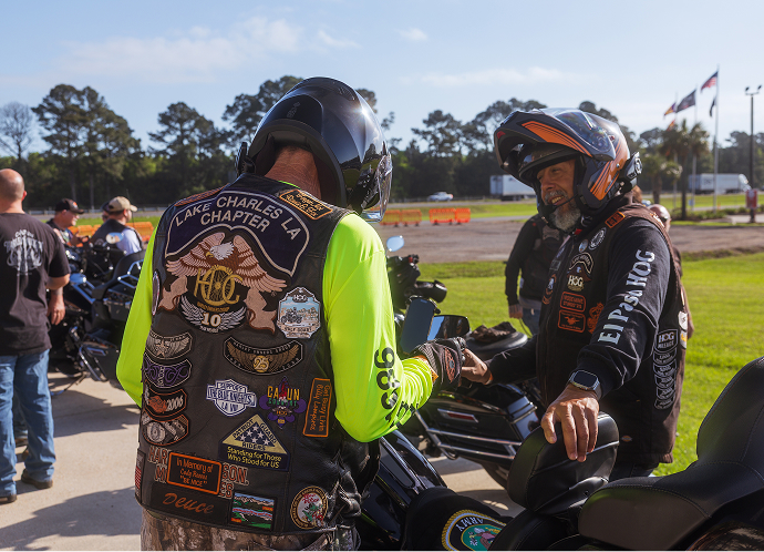 Several riders wearing club vests gather around parked motorcycles, talking before heading out together