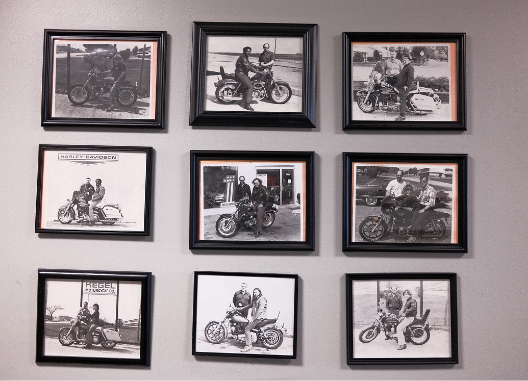 A wall of framed vintage black and white photos of customers with their new motorcycles
