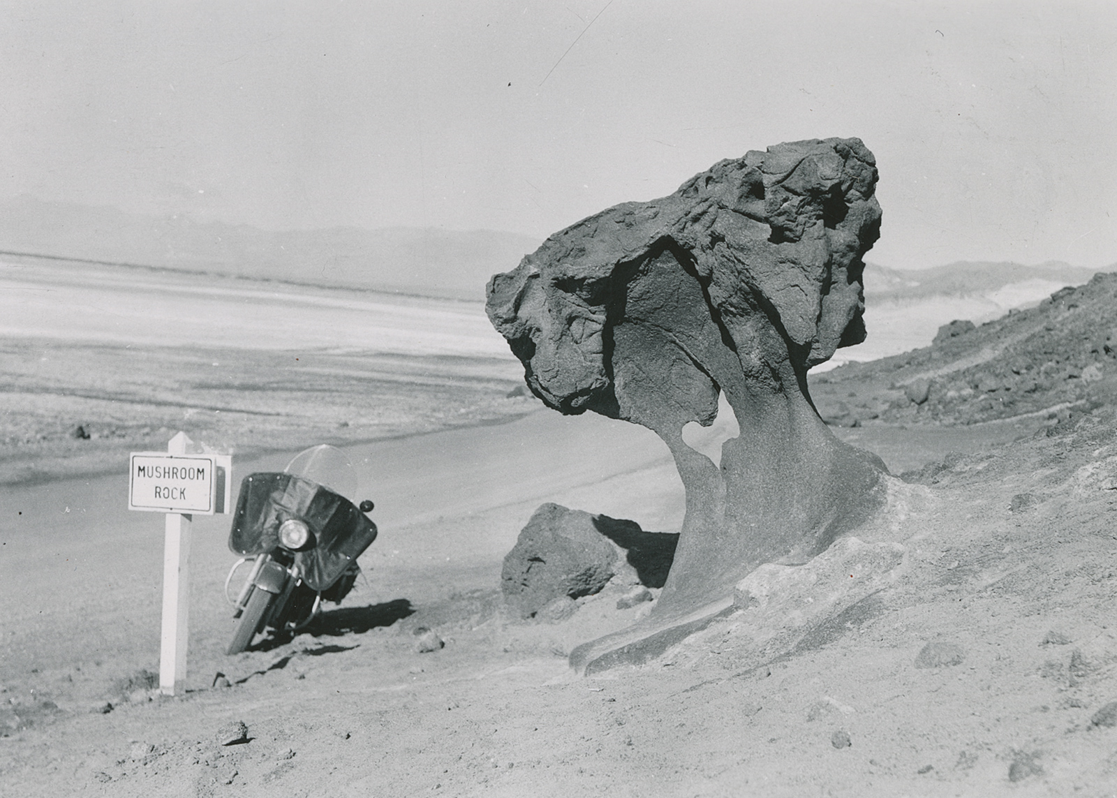 Black-and-white historical photo taken by Eldred Harrington of his 1951 hydra-glide in front of mushroom rock in death valley.