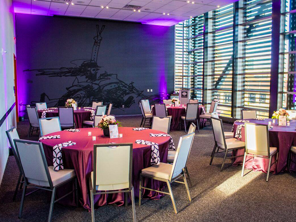 Round tables with purple linens in sunlit event room with large windows