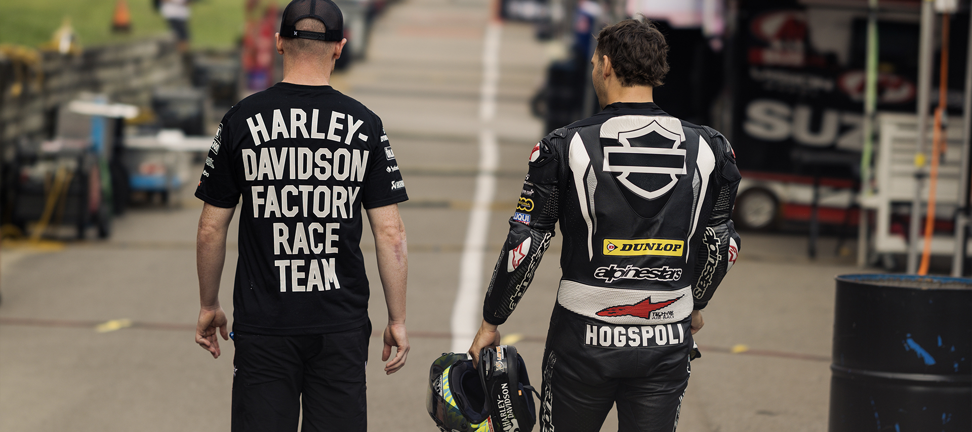 James Rispoli walks alongside a Harley-Davidson Factory Race Team member, holding his helmet after the race.