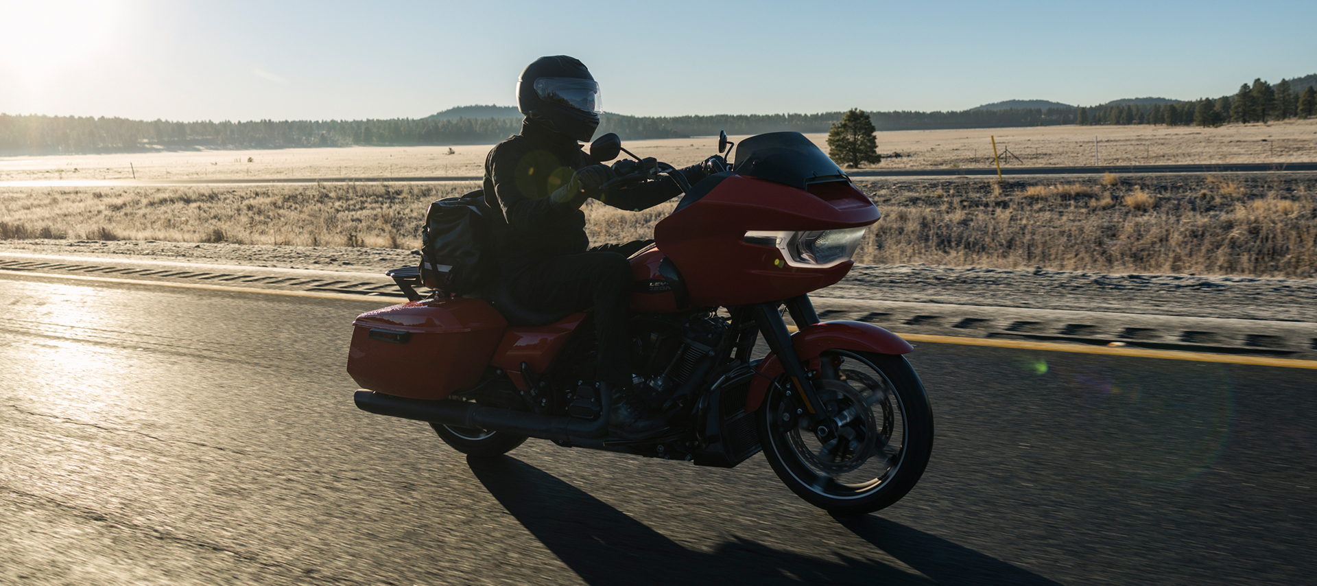 A rider on a Harley-Davidson Road Glide travels along a frosty stretch of Route 66 with the sun low over the horizon