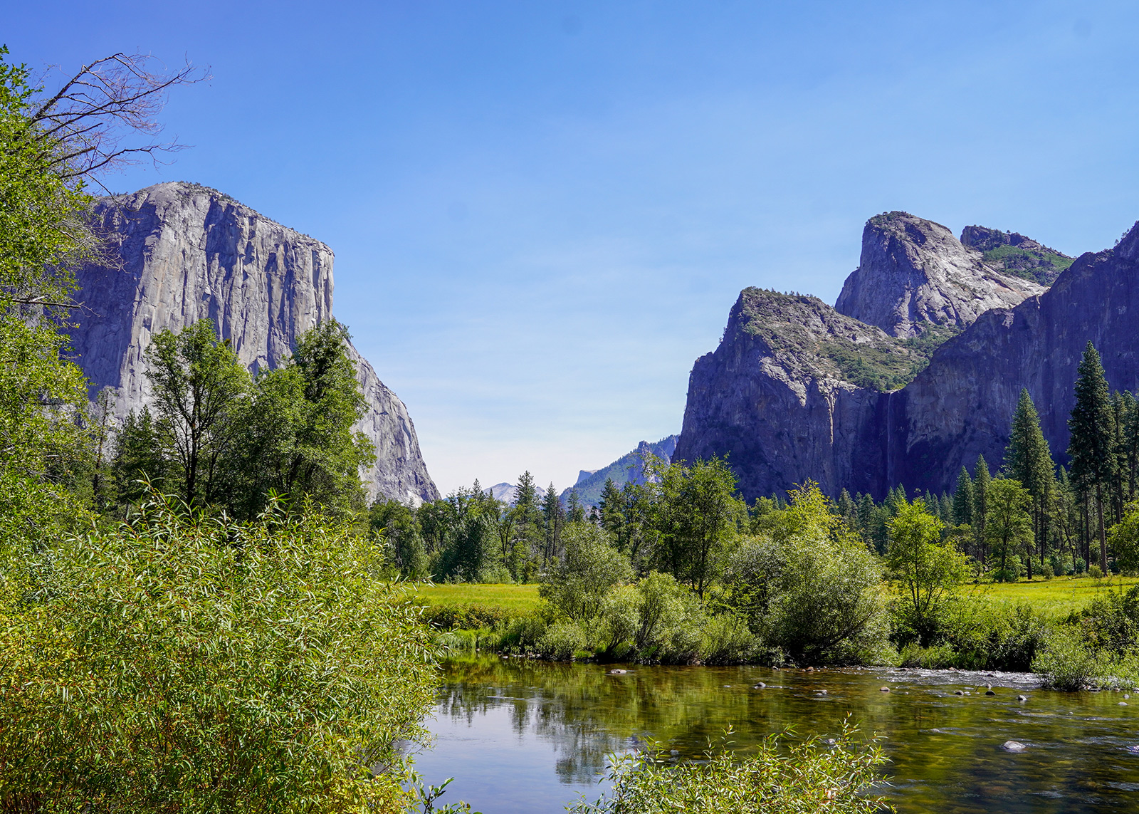 View of El Capitan and Cathedral Spires in Yosemite Valley with a river and trees in the foreground.