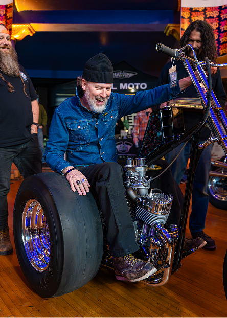 Person sitting on a custom chopper trike with drag racing tires at Mama Tried