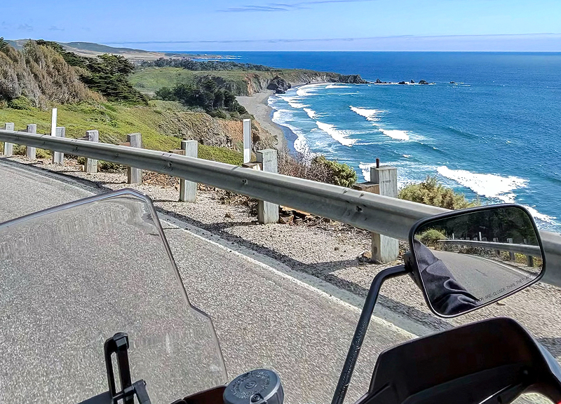 View from Red H-D Pan America motorcycle riding along coastal highway with guardrail and waves below