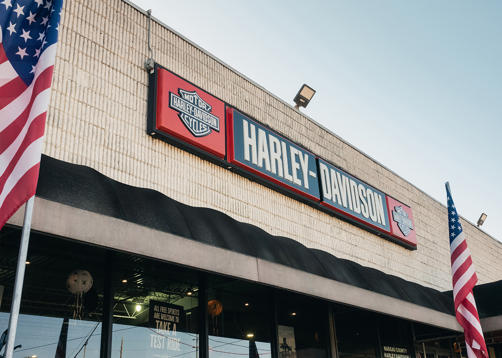 Looking up at the exterior signage of Harley-Davidson of Nassau County dealership with American flags on either side.