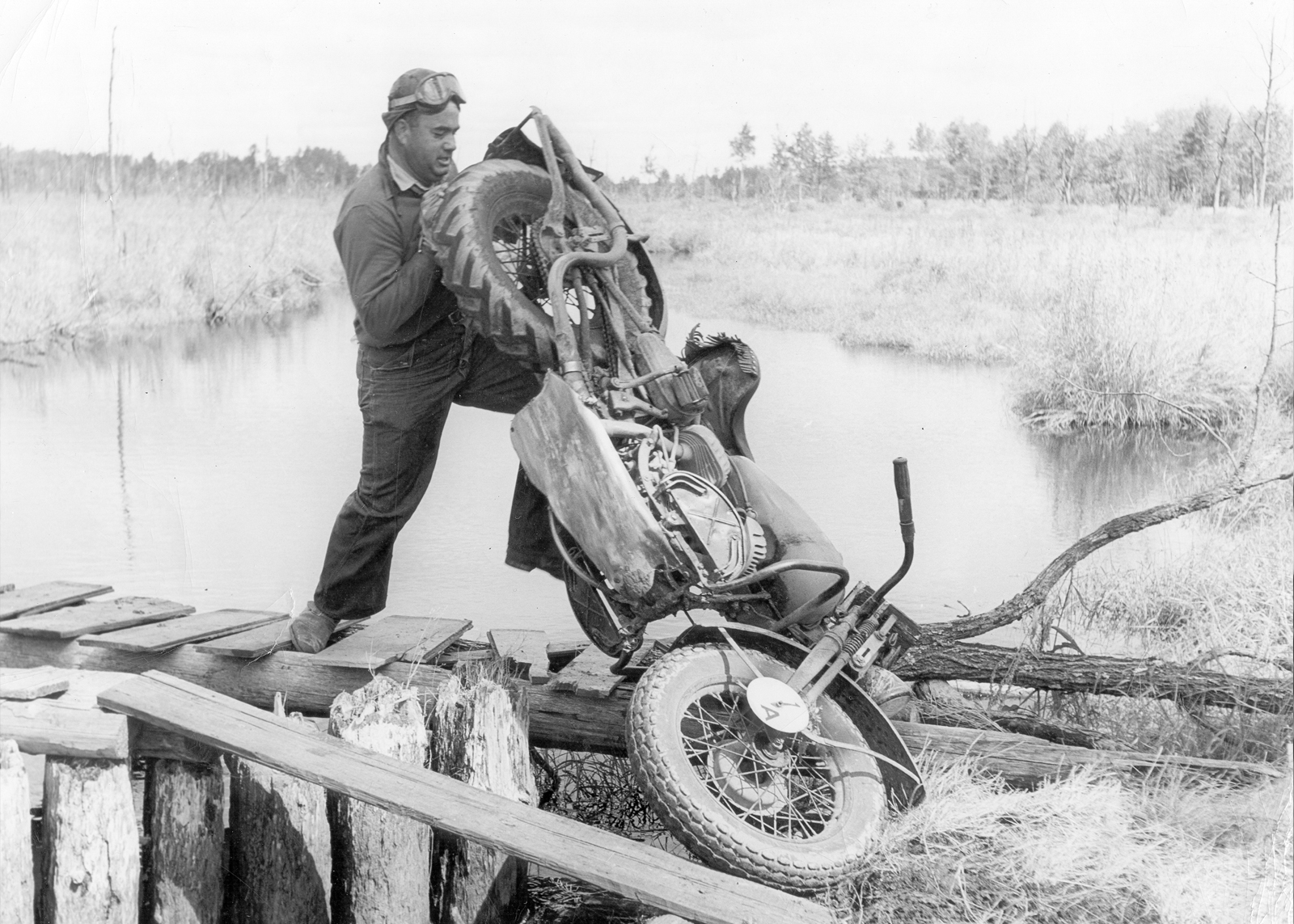 A soldier flips or rolls his H-D motorcycle over a wooden footbridge