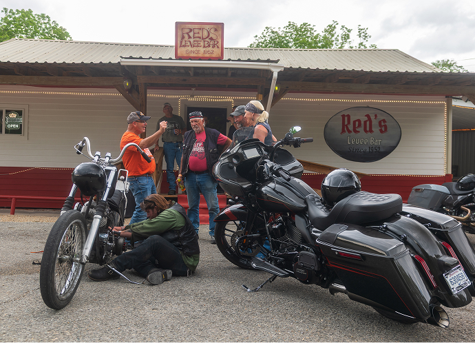 Motorcycles parked outside a small roadside restaurant as riders gather and chat on a sunny day