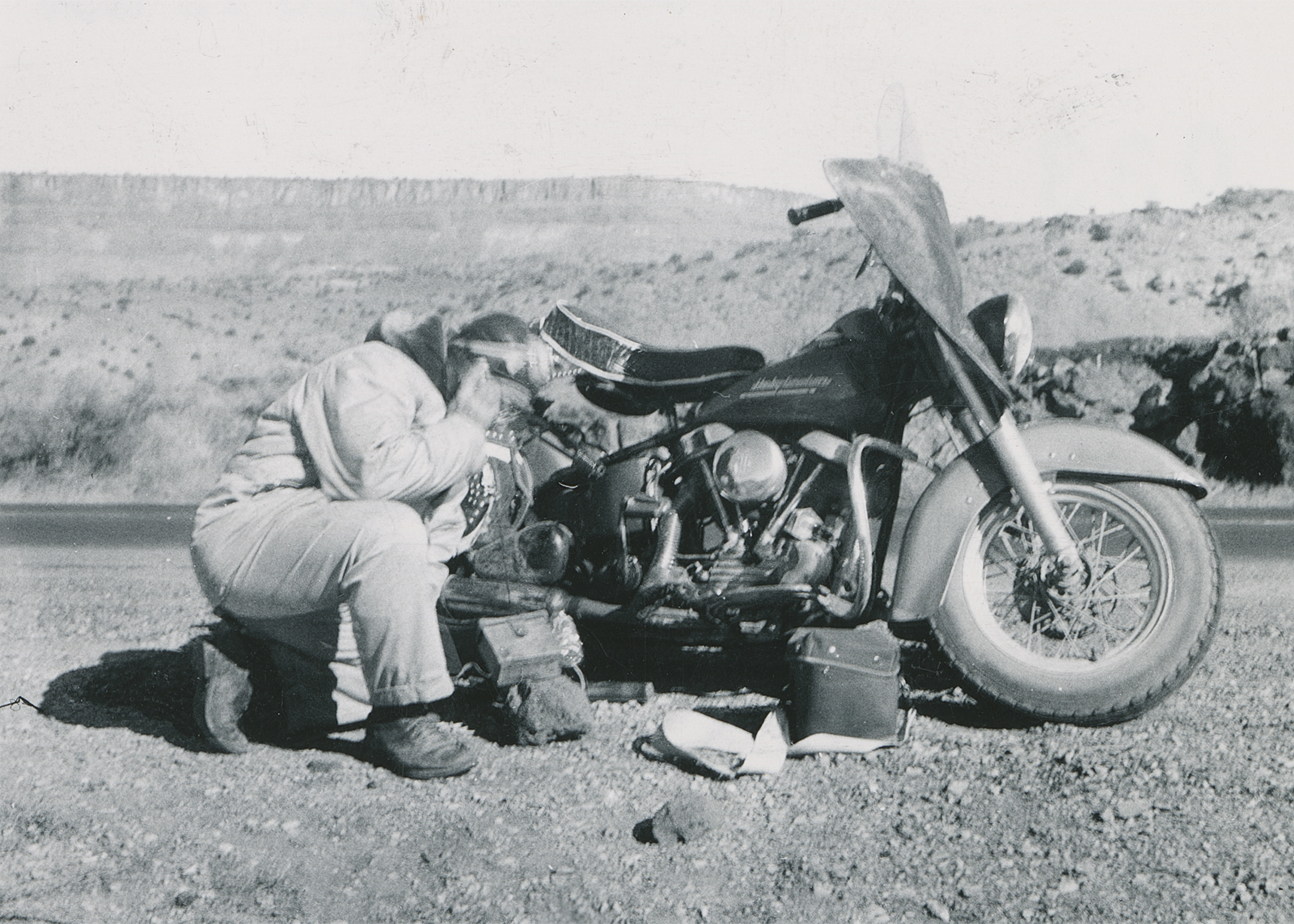 Black and white historical photo of Eldred Harrington with his 1951 Hydra Glide motorcycle by the side of the road using his homemade geiger counter.