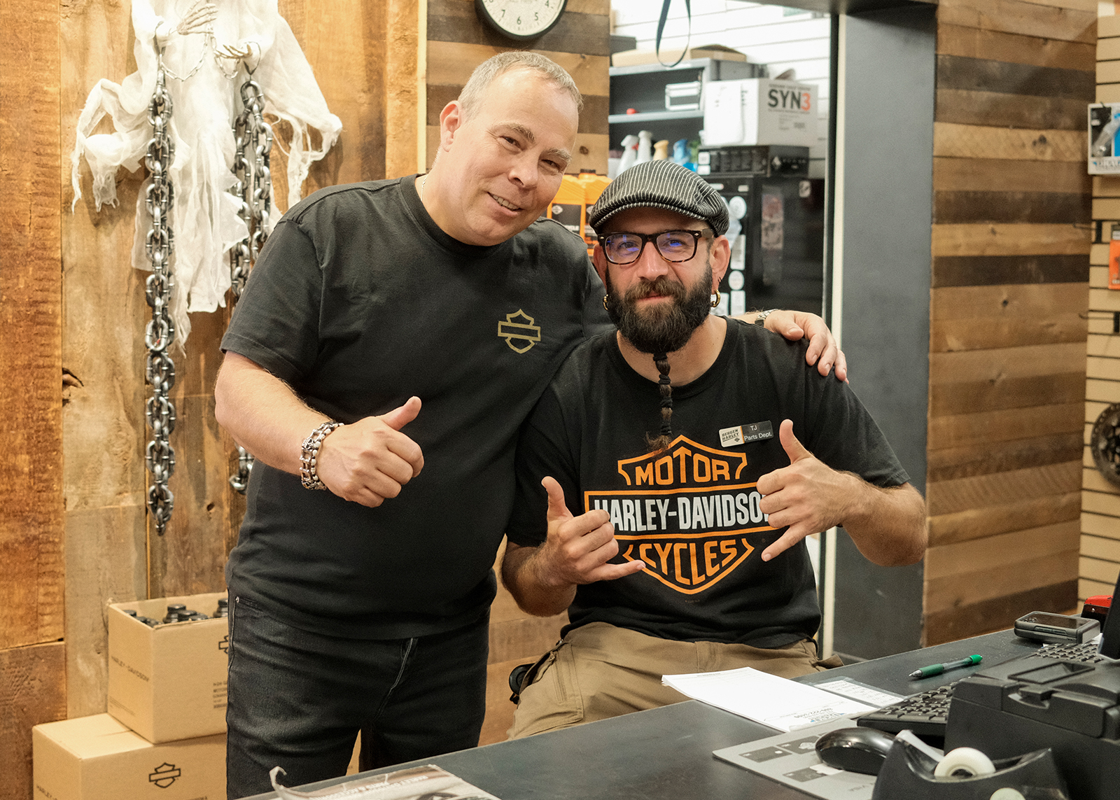 Two Bergen Harley-Davidson employees smiling at a counter, one giving a thumbs-up gesture.