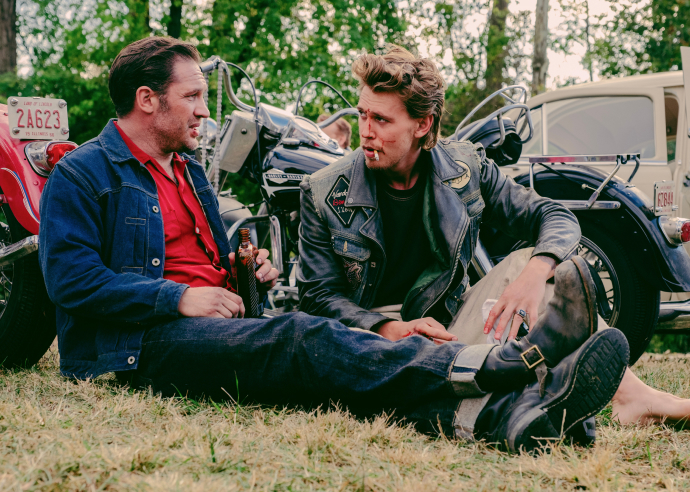 Tom Hardy as Johnny and Austin Butler as Benny sit on the grass 