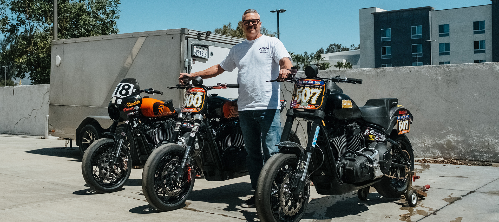 Brandon Quaid poses outside with three track prepped V-twin Harleys.