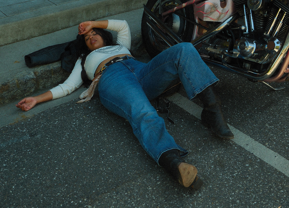 The author lays exhausted beside a custom chopper motorcycle parked along a curb on a paved downtown street