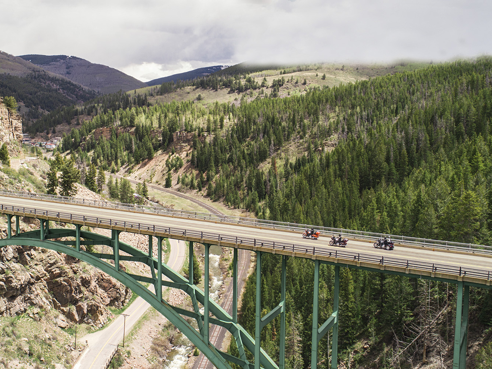 motorcycles riding down road over bridge