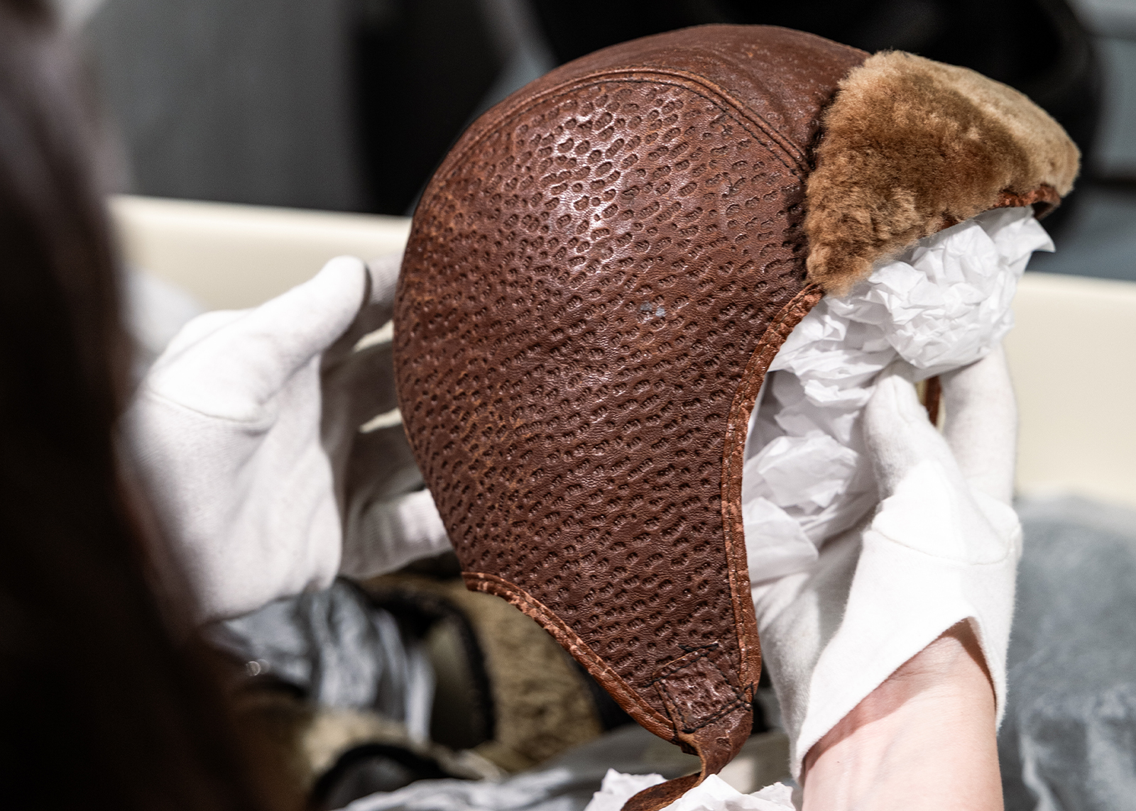 A museum archivist holds a vintage textured leather motorcycle helmet with a fur lined visor.