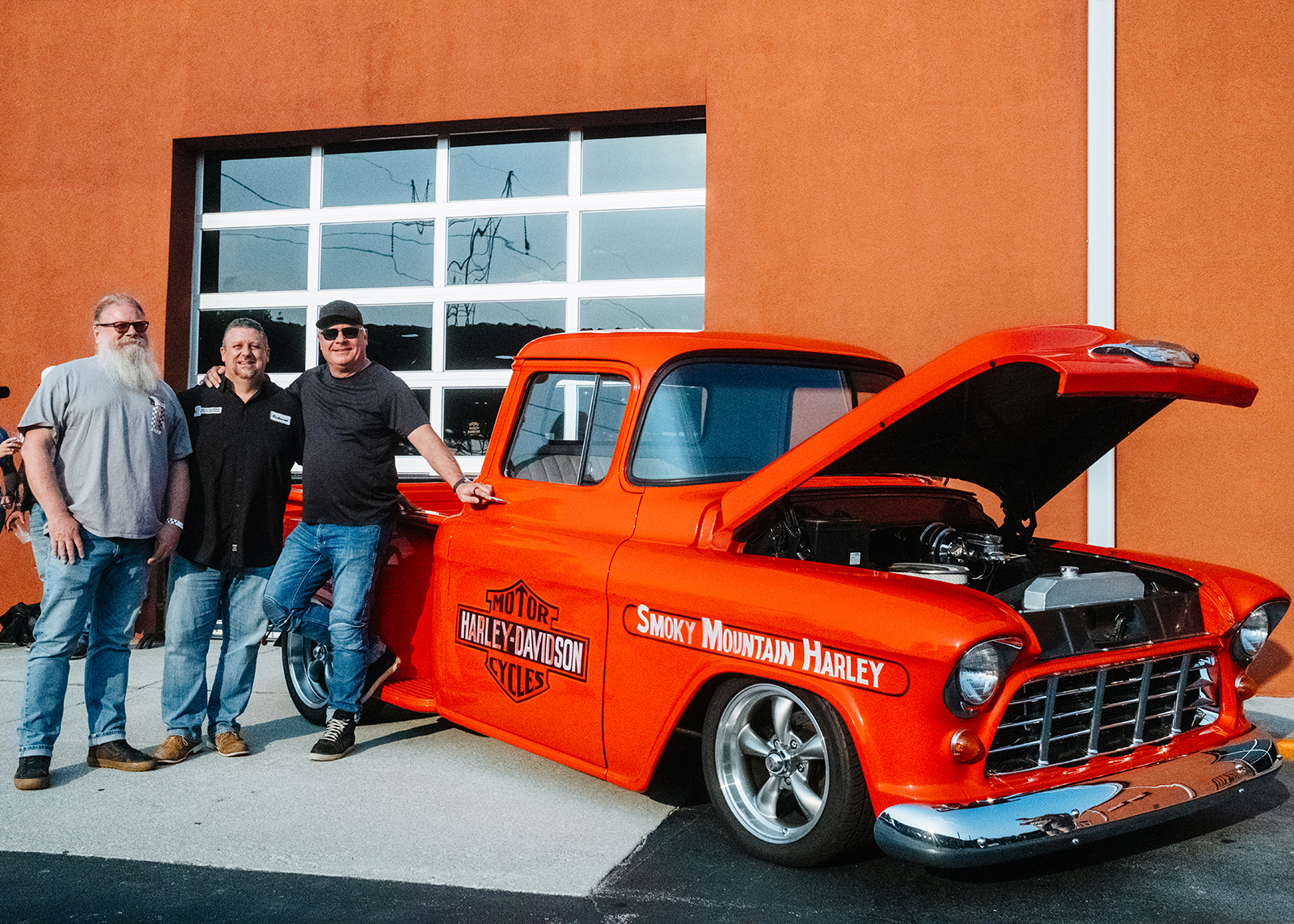 Three members of Smokey Mountain staff pose next to a restored vintage truck in front of the Smokey Mountain Harley-Davidson dealership.