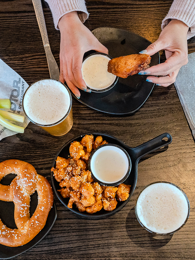 Overhead view of pretzel, fried bites, dipping sauce, and beer on table