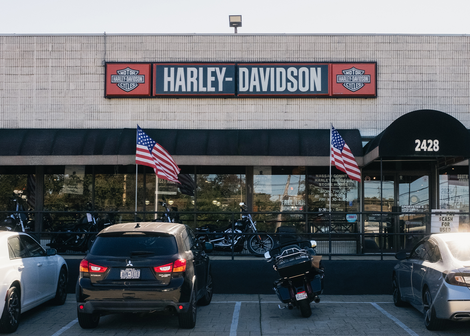 Exterior of Harley-Davidson of Nassau County dealership with parked vehicles and American flags lining the entrance.
