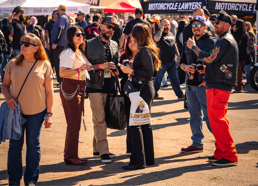 Crowd gathered near vendor tents at an outdoor motorcycle event on a sunny day