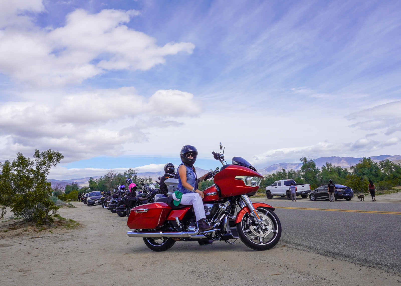 Woman in a denim vest sits on a Road Glide in a line of other bikes on the side of the road