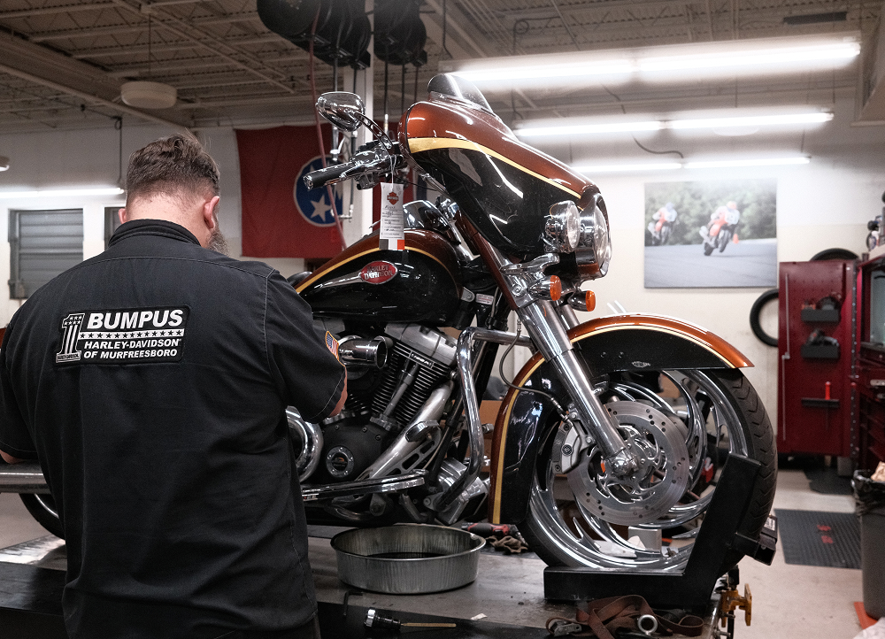 Technician adjusting a Harley-Davidson motorcycle mounted on a lift in a well-lit service bay